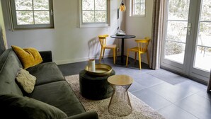 A cozy living room with a dark green sofa, a small round table with chairs, and a large window with curtains. - Romantic Loft w/ Garden Terrace (Ermelo)