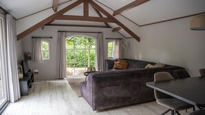 Ruime loft slaapkamer met groot raam, een donkere bank, een eettafel en houten balkenplafond.