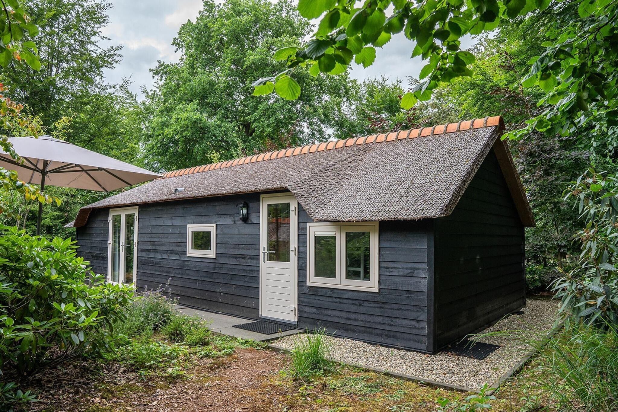 A small, dark wooden cabin with a tiled roof, surrounded by lush greenery.