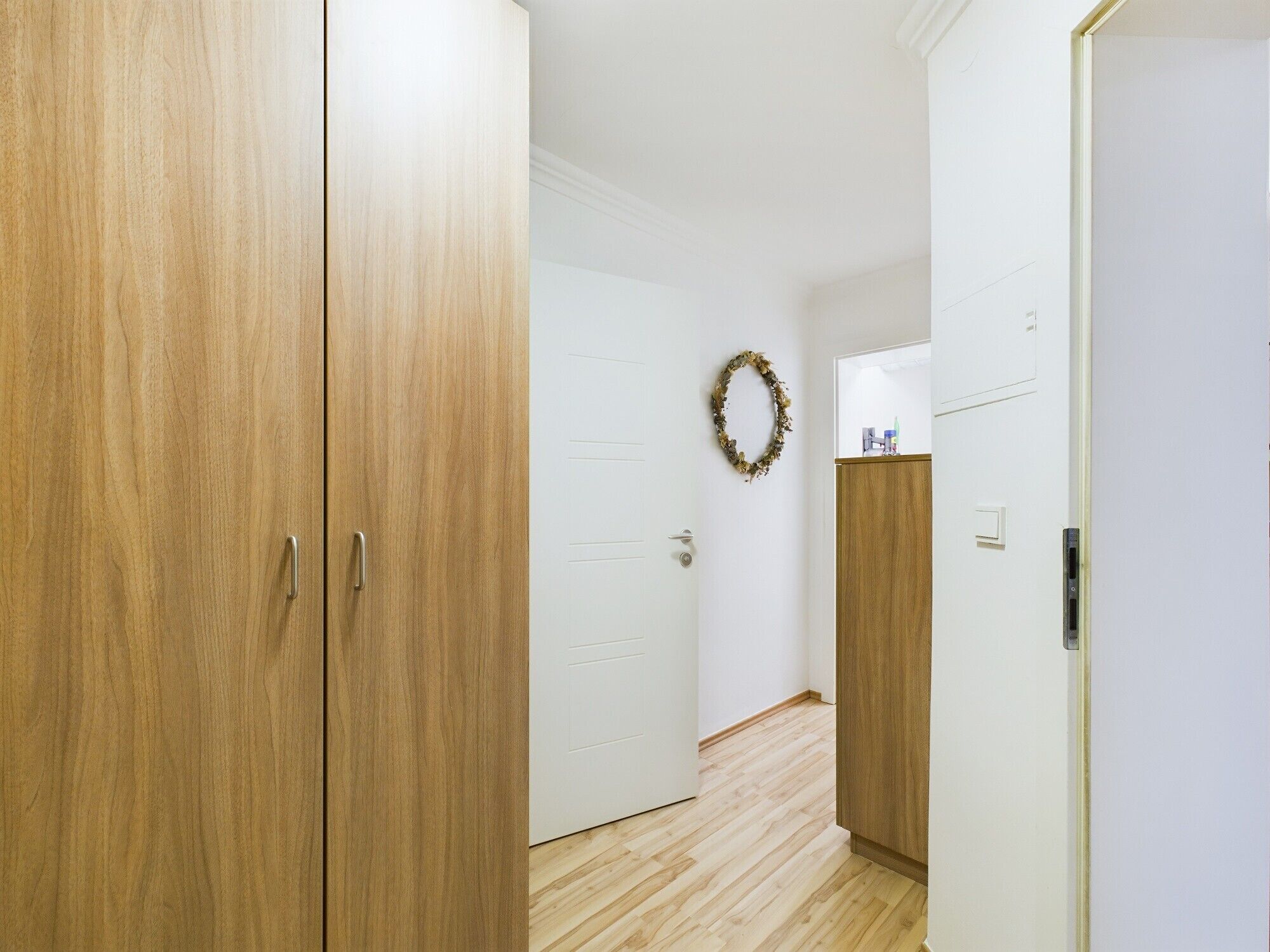 A hallway with wooden doors, a white wall, and a wooden floor.
