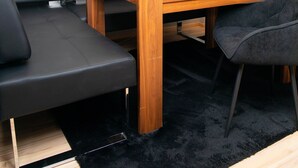 Een moderne kamer met een houten eettafel, een zwarte leren bank en een pluizig zwart tapijt.