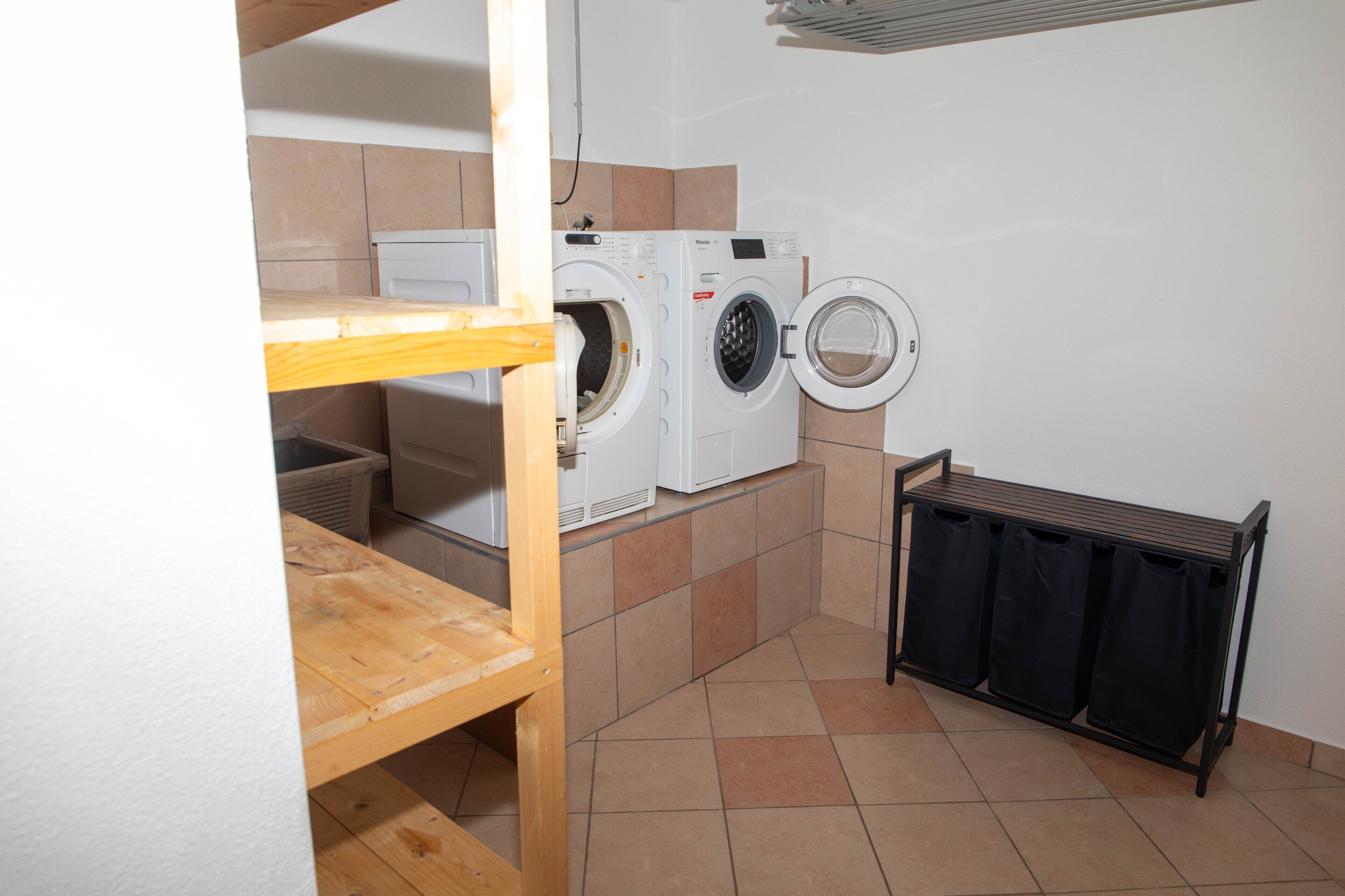 A laundry room with two washing machines, a drying rack, and a radiator.