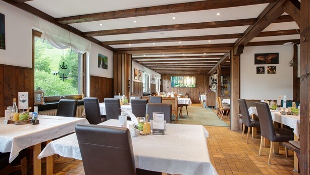 Ein Restaurant mit Holzbalken, weißen Tischdecken und Blick auf Grün.