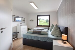 A bedroom with a bed, bedside lamp, window with a view, and a dresser.