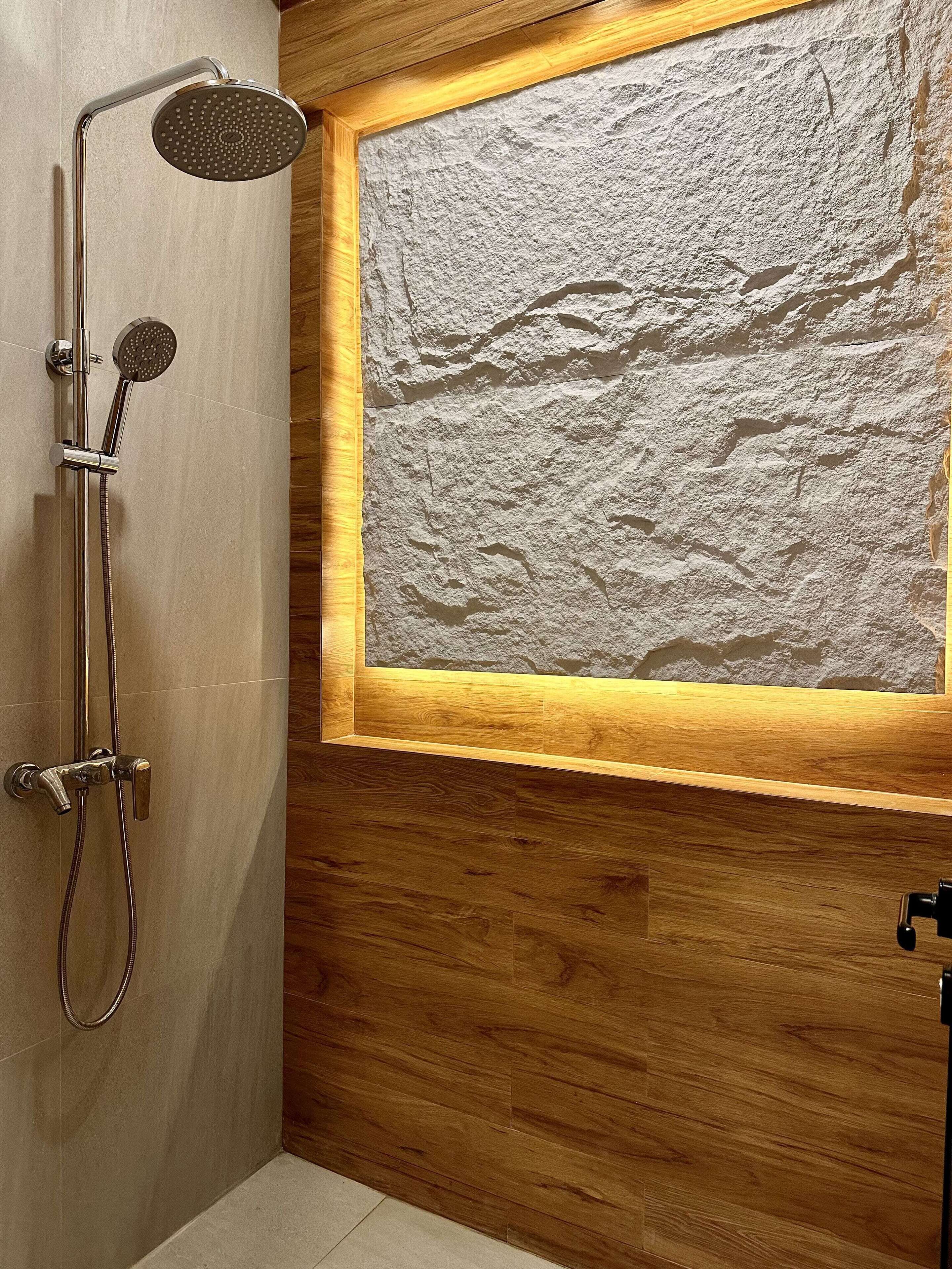 A modern bathroom with a shower, a wooden panel wall, and a textured stone-like wall feature.