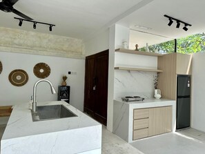 A modern kitchen with a marble countertop, a built-in sink, wooden cabinets, and a black refrigerator. - Spring Villa (Nusa Dua)
