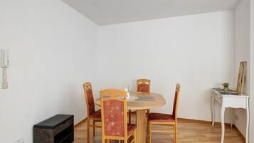 Een eetgedeelte met een ronde tafel, vier houten stoelen, een klein wit bureau met spiegel en een bank.
