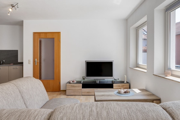 A modern living room with a sofa, a coffee table, a TV on a stand, a wooden door, and a window.