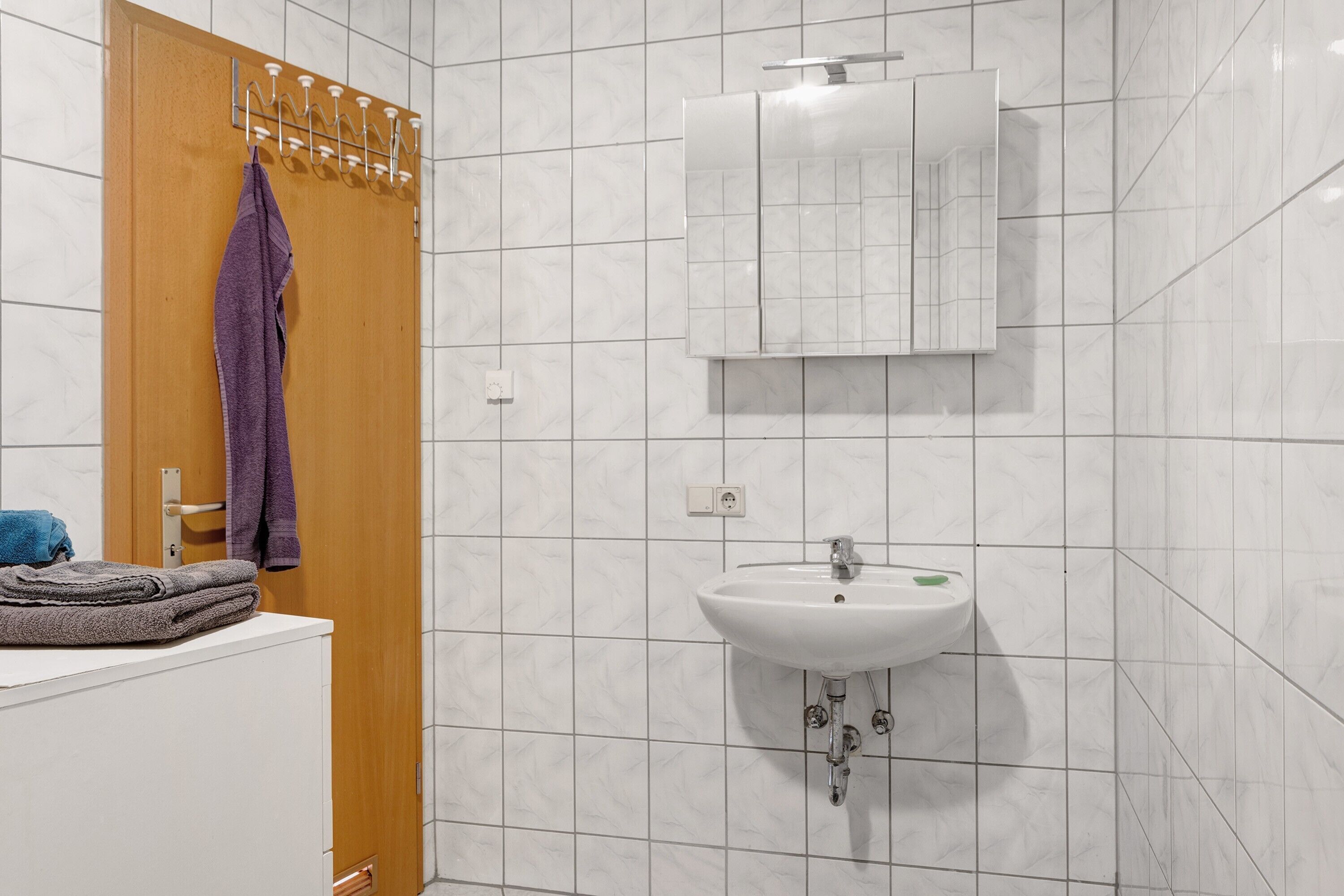 Een badkamer met een houten deur, een witte wastafel en een spiegel erboven.