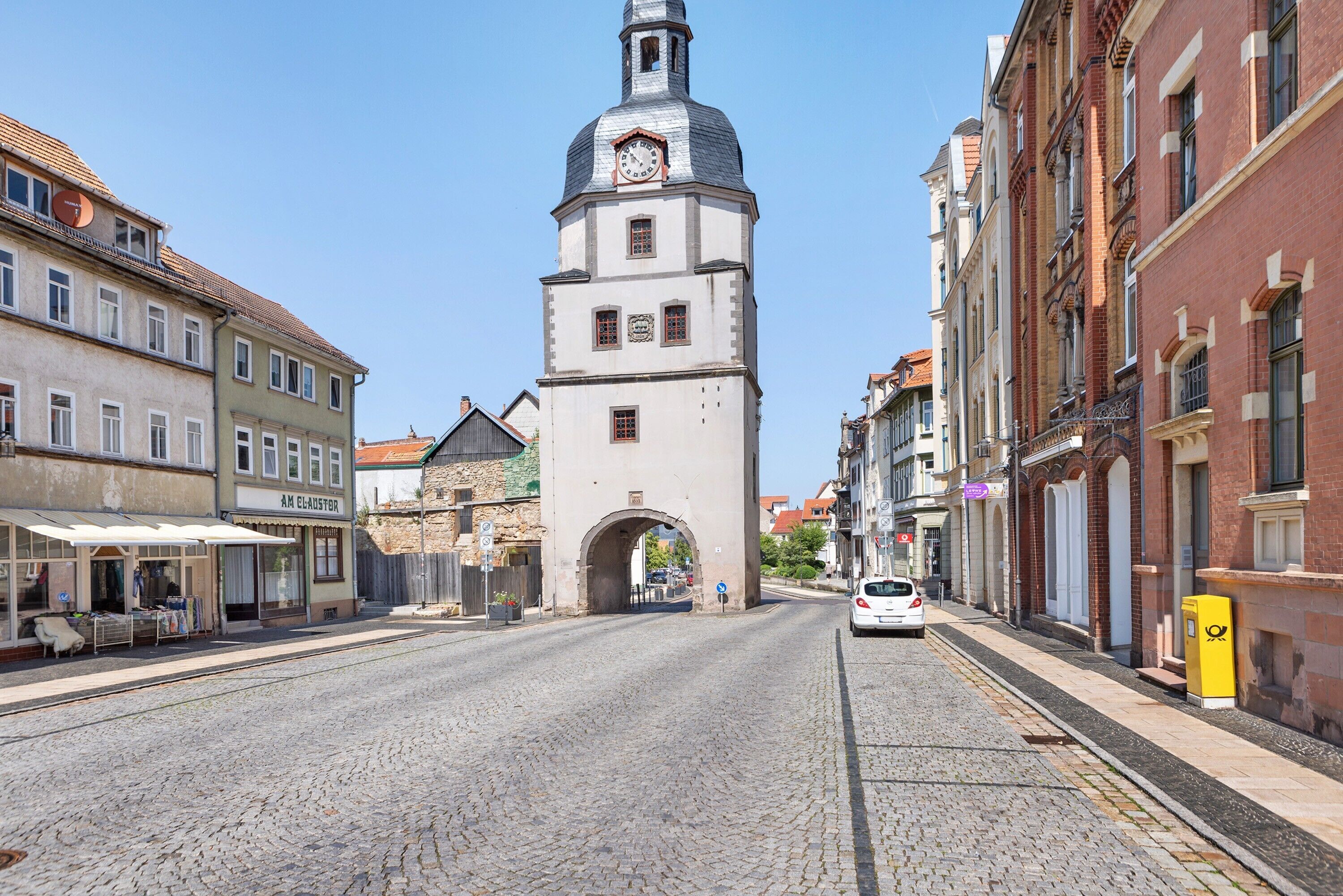 A cobblestone street with historic buildings, a clock tower, and a clear blue sky.