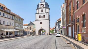 A cobblestone street with historic buildings, a clock tower, and a clear blue sky.
