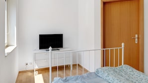 A bedroom with a bed, a TV on a white dresser, a wooden door, and a window.