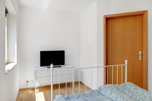 A bedroom with a bed, a TV on a white dresser, a wooden door, and a window.