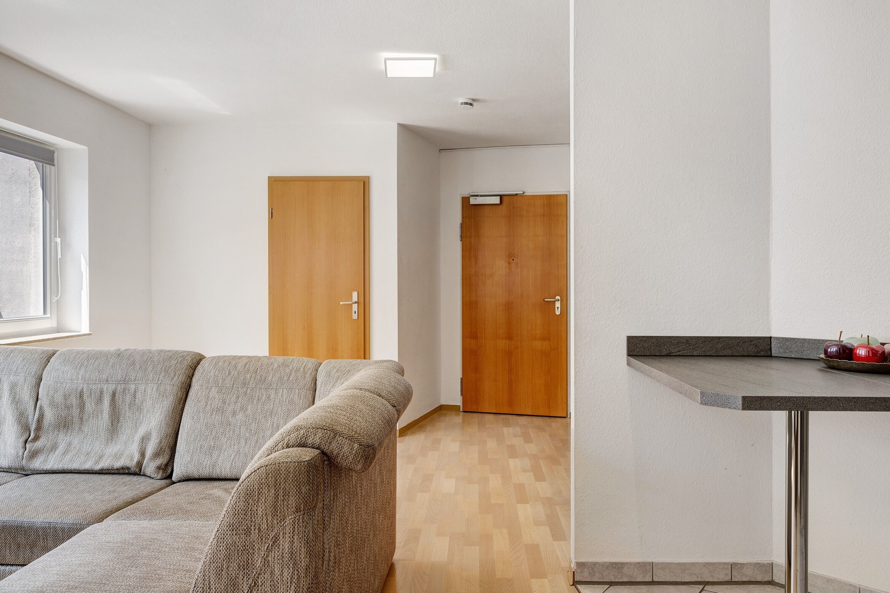 A modern living room with a sofa, wooden doors, and a kitchen counter with apples.
