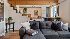 A modern living room with a grey sectional sofa, a small black side table, and a staircase leading to a kitchen area. - Apartment 'Rudemsmännchen' with Terrace and Garden (Eisenbach (Hochschwarzwald))