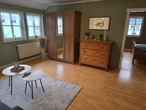 A room with a wooden cabinet, a small table, a radiator, and a window with a view.
