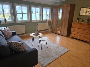A living room with a sofa, two small tables, a cabinet, and large windows.