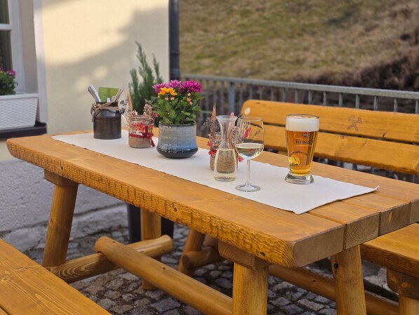 A wooden table with a white placemat, a glass of beer, a glass of white wine, and a potted plant with flowers.