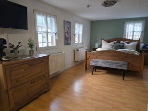 Una camera da letto con un letto di legno, un comodino, una cassettiera, un termosifone e una finestra con tende.
