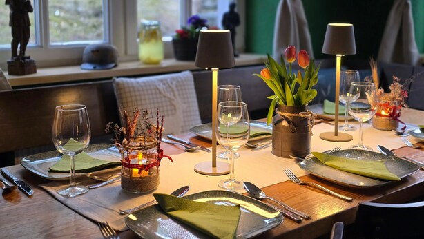 A dining table set with plates, cutlery, and glasses, a candle in a jar, and a vase with flowers. - Room 'Rote Pockau' with Mountain View and Wi-Fi (Marienberg OT Pobershau)