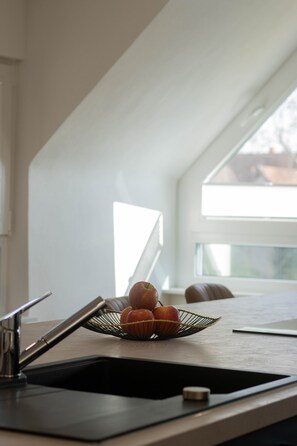 Une cuisine équipée d’un évier, d’un panier de fruits contenant des pommes et d’une fenêtre donnant sur un beau paysage.