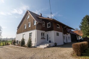 Une maison à deux étages, avec un toit en pente, un porche à l’avant et une allée gravillonnée.