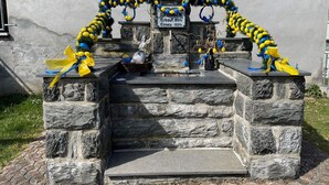 A stone memorial with a sign, decorated with blue and yellow ribbons and a rabbit statue.