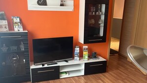 A modern living room with a flat-screen TV, a shelf with a decorative item, a cabinet with glassware, and a sign that reads 'HOME'.
