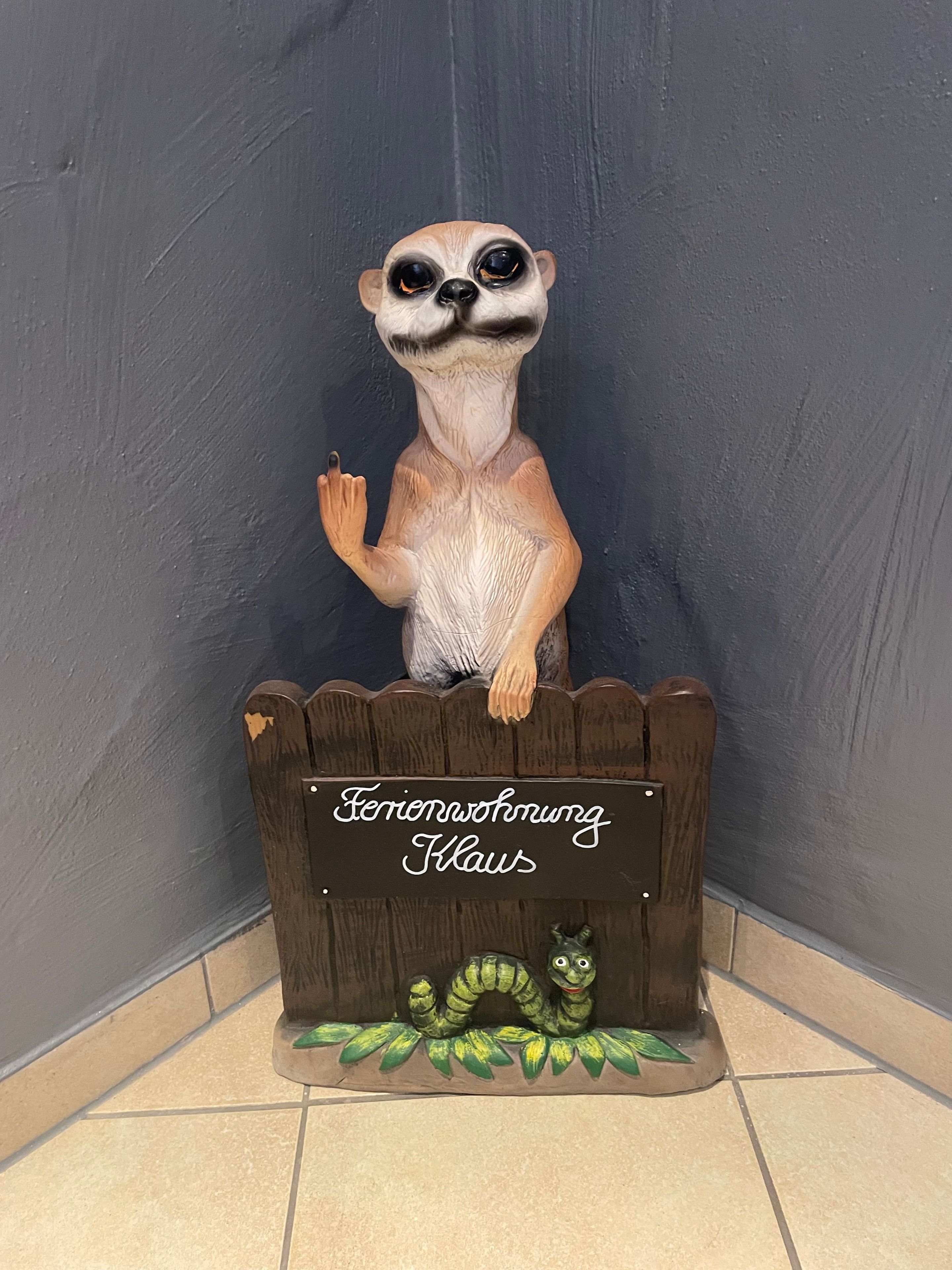 Een decoratief dierenbeeldje voor een houten hek met een bordje waarop 'Ferienwohnung Klaws' staat.