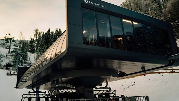 A modern ski lift station with a prominent 'Doppelmayr' sign, metal railings, and a snowy landscape with trees in the background.