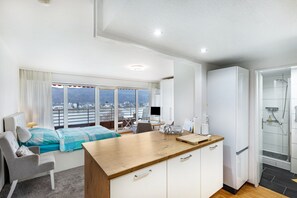 Una habitación de hotel moderna con balcón, cama, escritorio, refrigerador y zona de ducha.