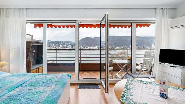 Ett hotellrum med en balkong, en säng, en TV och ett fönster med utsikt över staden.