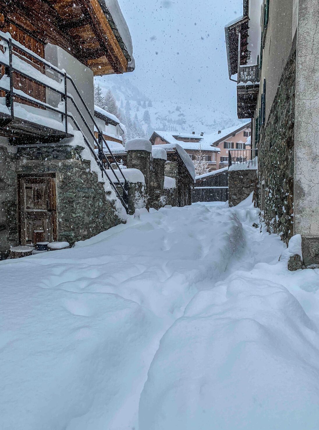 Une rue enneigée bordée d’immeubles en pierre, de balcons en bois et d’une atmosphère rustique.