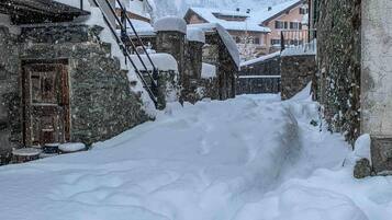 Une rue enneigée bordée d’immeubles en pierre, de balcons en bois et d’une atmosphère rustique.