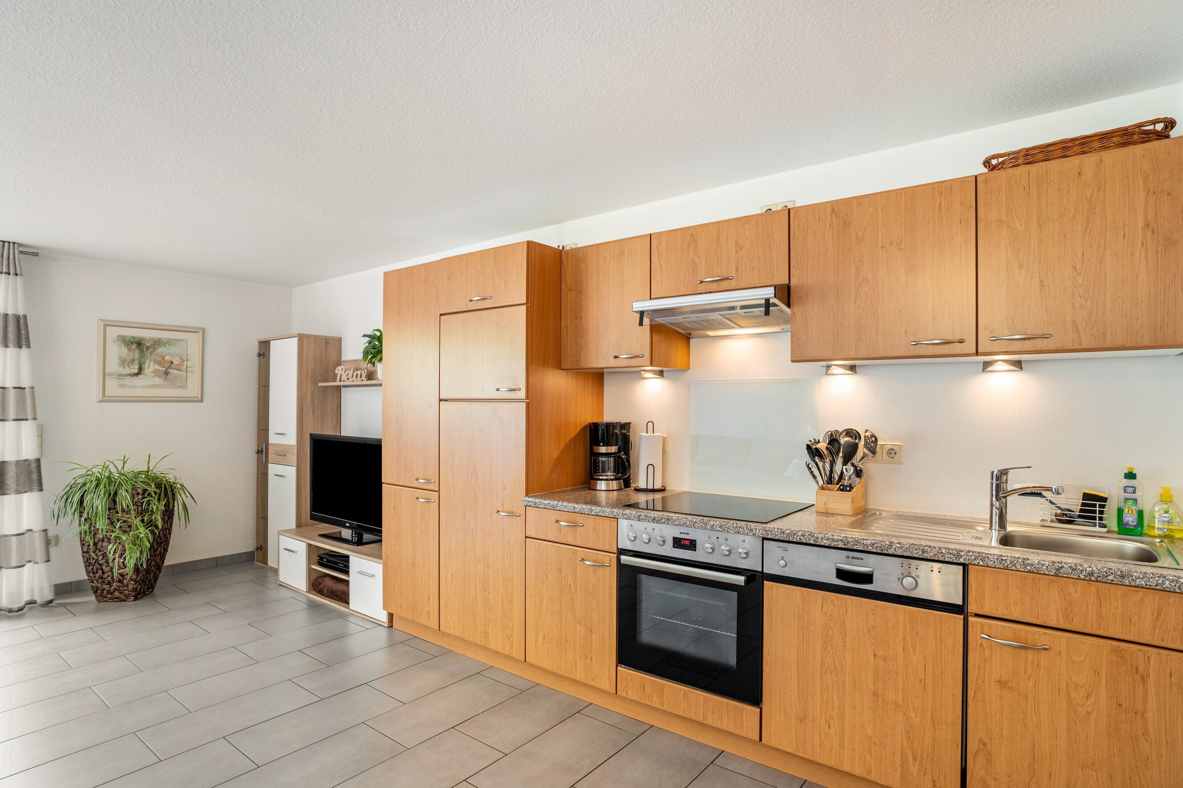 A modern kitchen with wooden cabinets, a built-in oven, a coffee maker, and a sink.