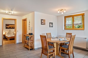 A dining area with a wooden table and chairs, a bookshelf, and a window with curtains.