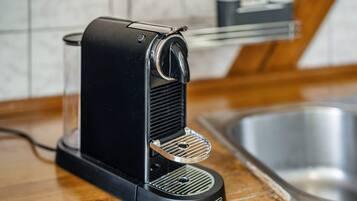 A black coffee machine on a wooden countertop with a stainless steel sink in the background.