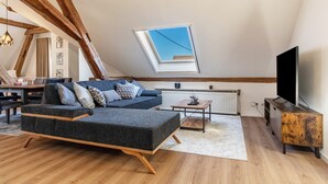 Un salón estilo loft con techo inclinado, un sofá seccional, un televisor, una mesa de centro de madera y un radiador.