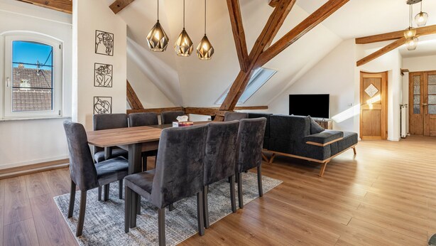 Un apartamento estilo loft con vigas de madera a la vista, una mesa de comedor con sillas, un sofá y un televisor.