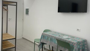 A small, modern room with a flat-screen TV mounted on the wall, a table with chairs, and a bench. - Charming double room with extra bed in delightful Roma with WiFi, AC (Roma)