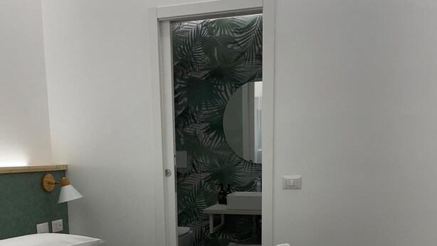A neatly made bed with rolled towels, a bedside lamp, and a view of a bathroom through a door with a palm leaf pattern. - Charming double room with extra bed in delightful Roma with WiFi, AC (Roma)