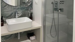 A modern bathroom with a glass-enclosed shower, a white sink, and a large mirror with a leaf-patterned backsplash. - Charming double room with extra bed in delightful Roma with WiFi, AC (Roma)