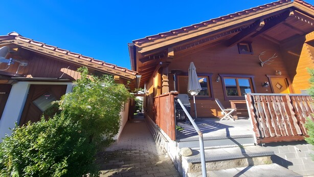 A wooden chalet with a covered patio, a staircase, and a view of the surrounding landscape. - Chalet Finkennest: Mountain Views, Private Terrace, Peaceful Location in Neukirchen (Neukirchen am Großvenediger)