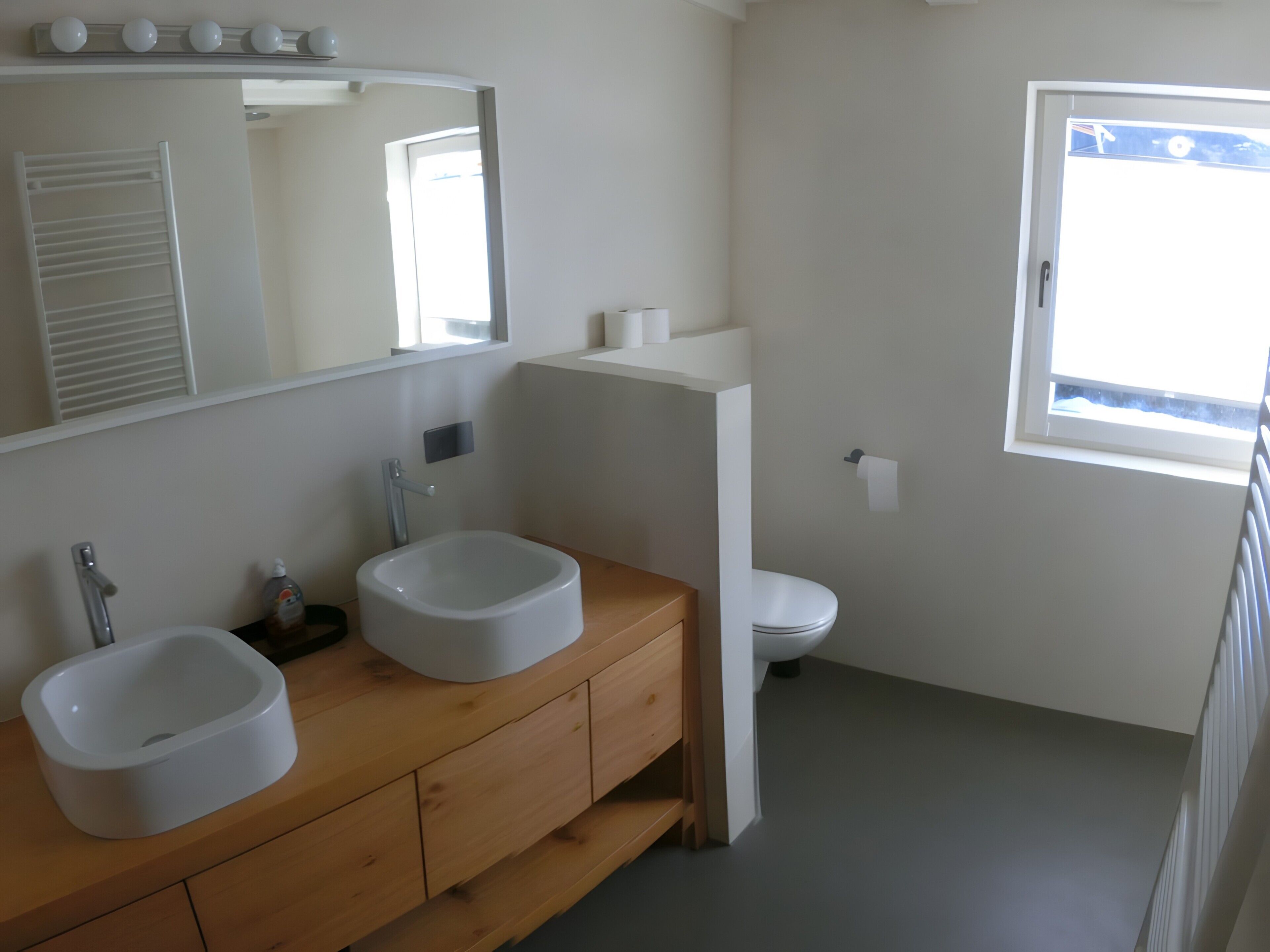 Bagno con due lavandini, un water, uno specchio e una finestra.