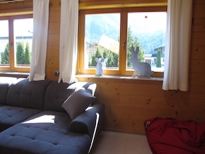 A room with a sofa, a window with curtains, and a view of mountains.