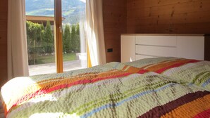 A bedroom with a large window, wooden walls, a bed with a colorful quilt, and a white headboard. - Chalet Finkennest: Mountain Views, Private Terrace, Peaceful Location in Neukirchen (Neukirchen am Großvenediger)