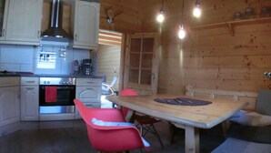 A wooden interior with a kitchen area featuring cabinets, a stove, and a dining table with chairs. - Chalet Finkennest: Mountain Views, Private Terrace, Peaceful Location in Neukirchen (Neukirchen am Großvenediger)