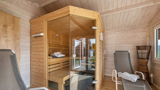 Ein Saunaraum mit Holzwänden, einer Glastür, einer Sitzbank und zwei Liegestühlen.