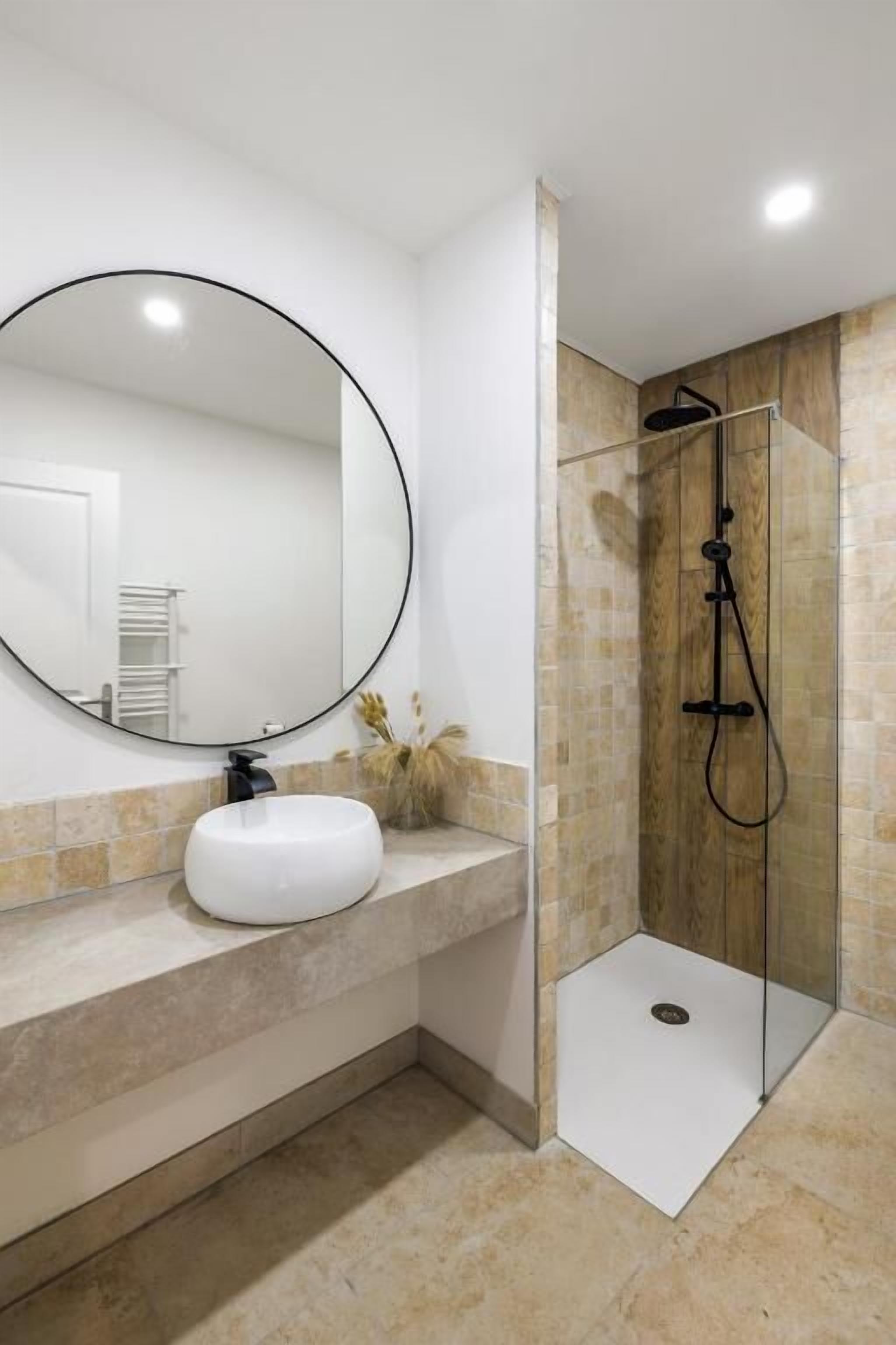 Un bagno con uno specchio rotondo, un lavandino bianco e una cabina doccia in vetro.