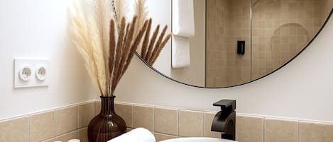 A bathroom with a white sink, a mirror, a towel, and a vase with pampas grass.